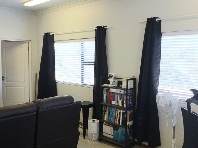 A living room area featuring tiled flooring, multiple windows with venetian blinds, and a standard interior door.