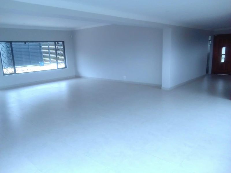 A spacious, open-plan living area featuring neutral tiled flooring, recessed lighting, and large windows with security bars.