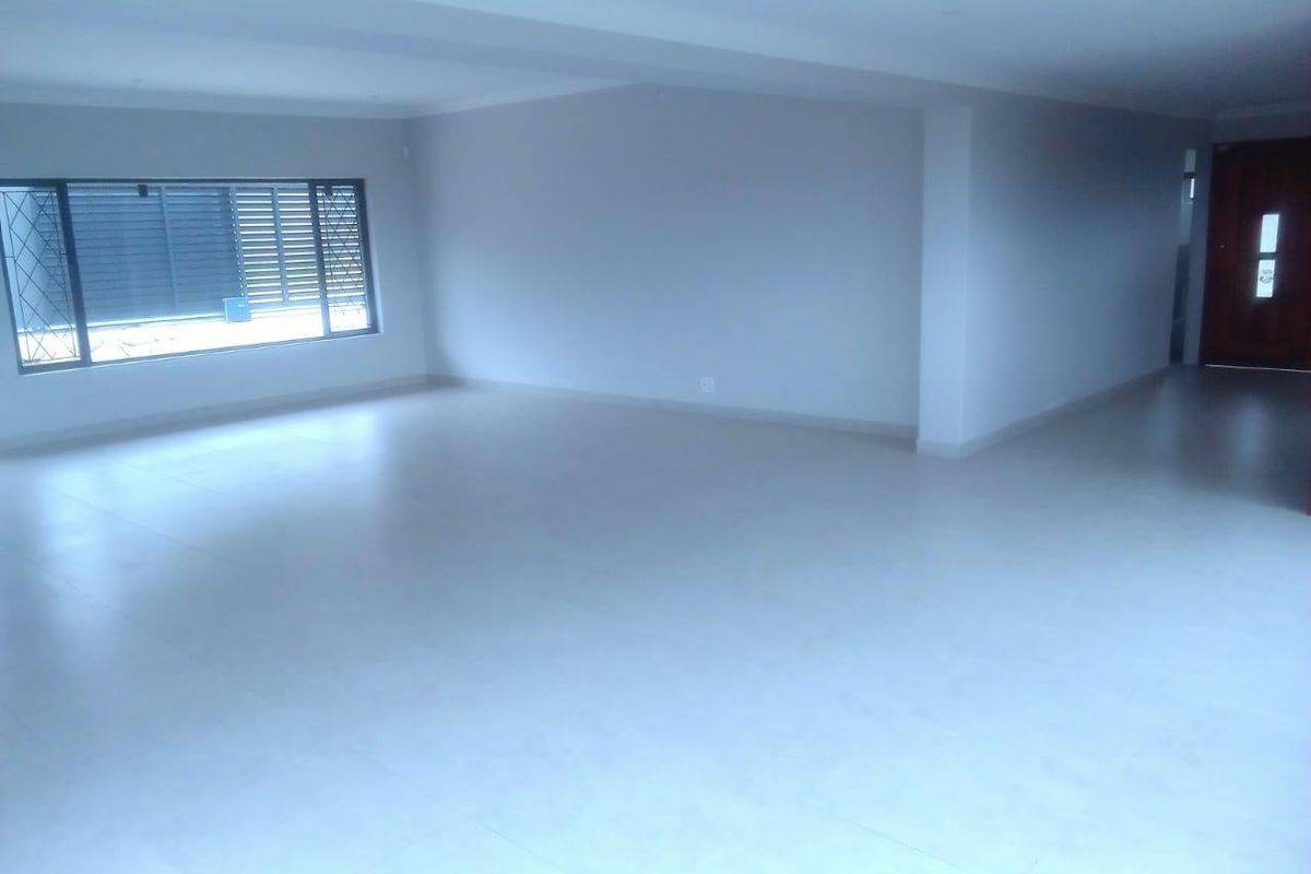 A spacious, open-plan living area featuring neutral tiled flooring, recessed lighting, and large windows with security bars.