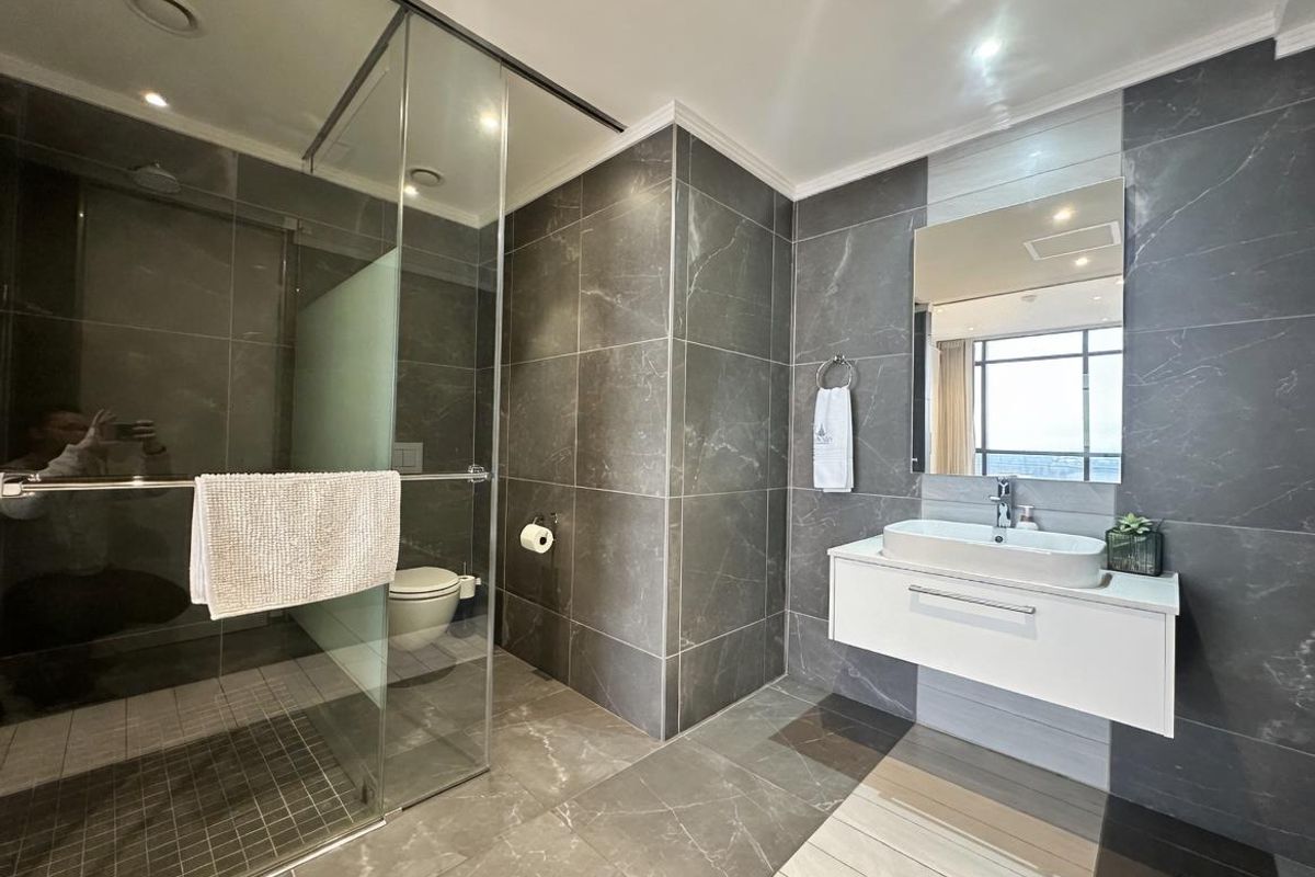 Modern bathroom featuring dark marble-effect wall and floor tiles, a floating vanity with a vessel sink, and a glass-enclosed walk-in shower.