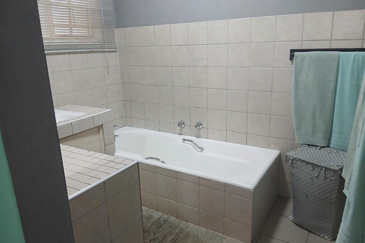 A functional bathroom featuring a built-in bathtub with tiled surround, wall-mounted taps, and a tiled vanity area.