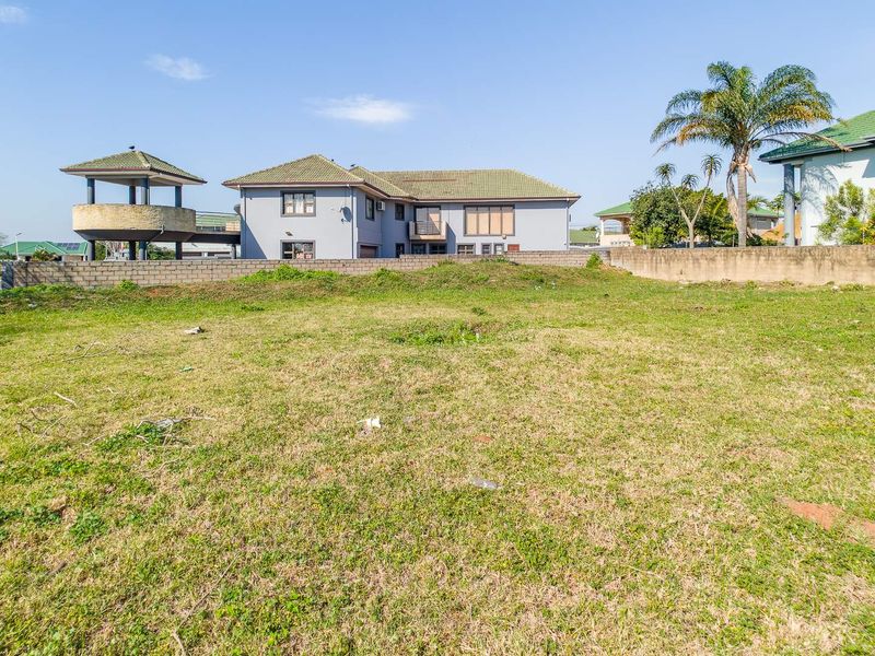 A vacant residential plot featuring a grass lawn and perimeter boundary wall, situated in a developed neighborhood.