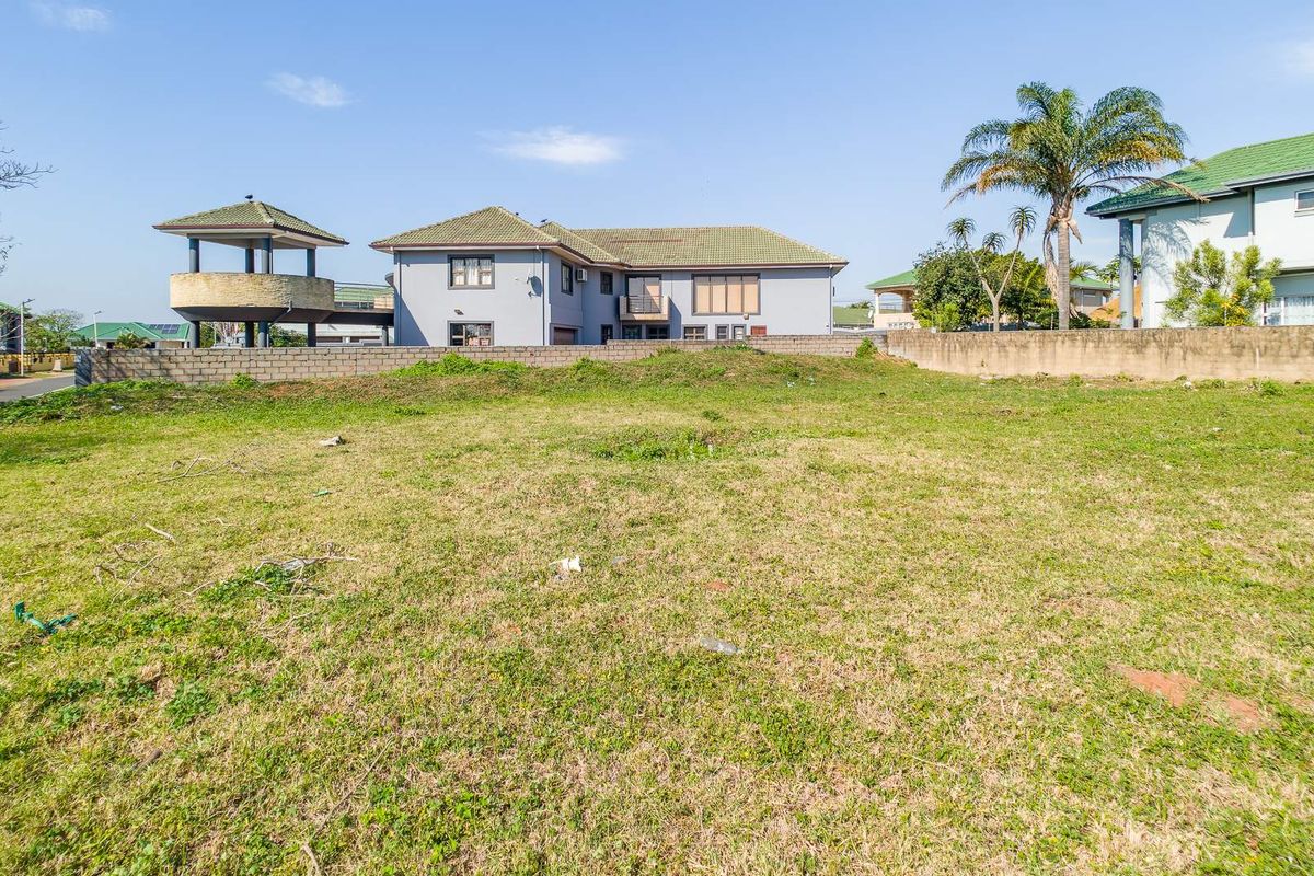 A vacant residential plot featuring a grass lawn and perimeter boundary wall, situated in a developed neighborhood.