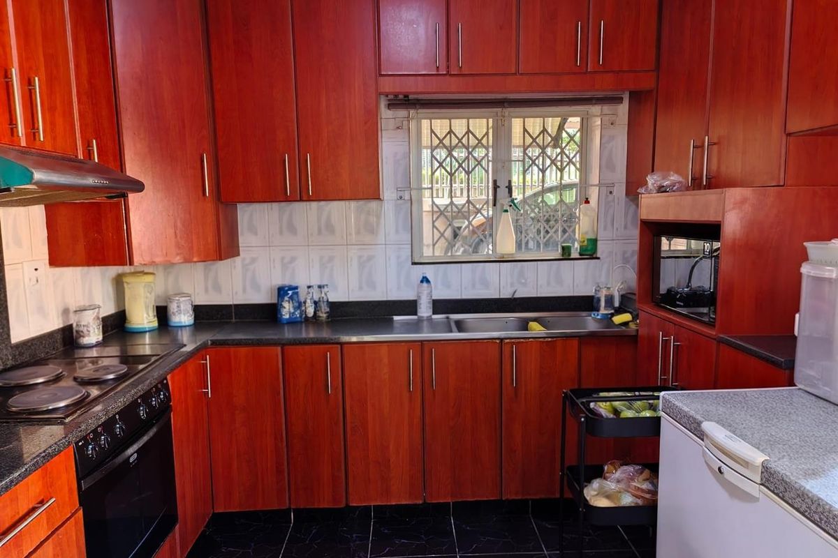 A functional kitchen featuring dark wood-look cabinetry, granite-style countertops, a built-in oven and hob, and a window with security bars.