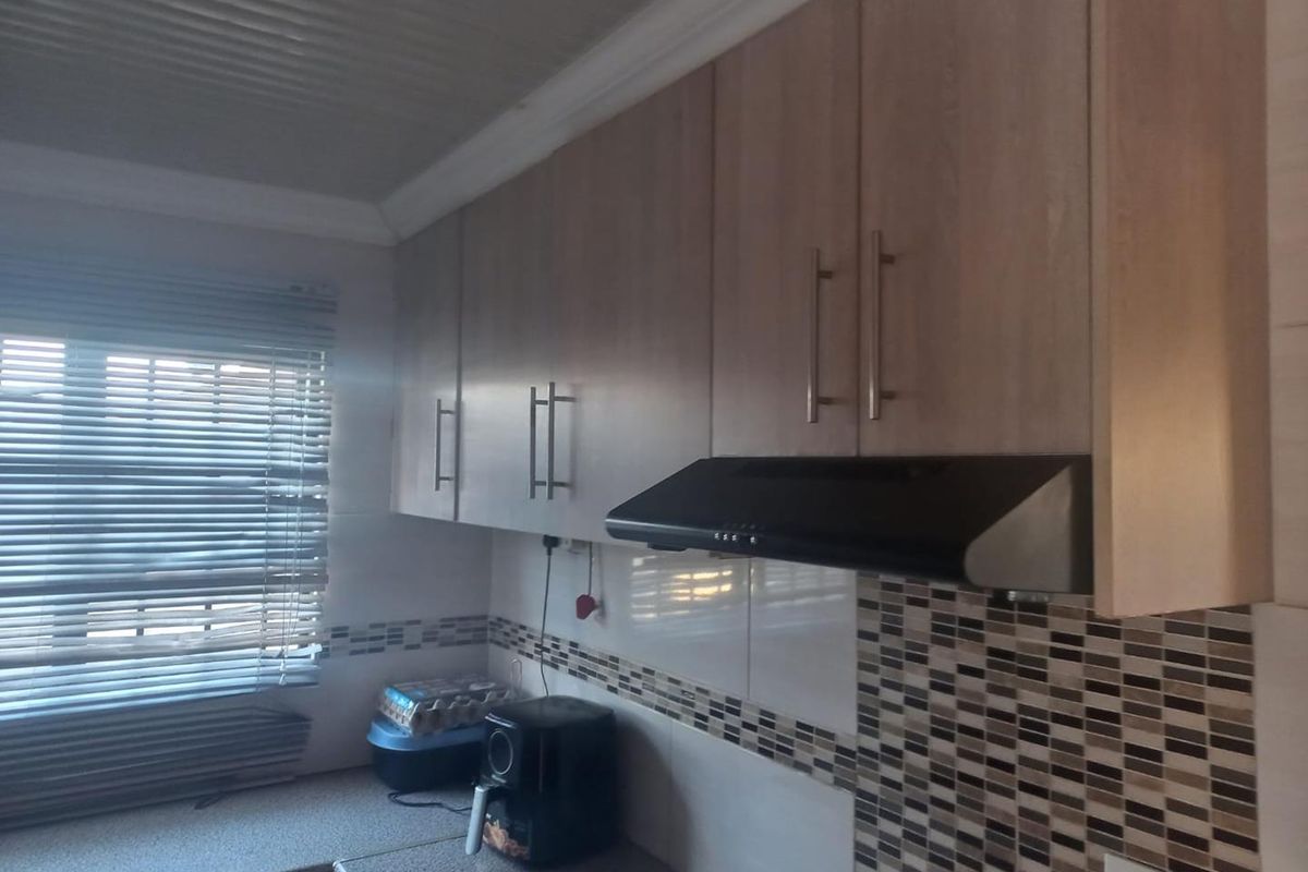 A functional kitchen area featuring light wood-tone cabinetry, a mosaic tile backsplash, and a built-in extractor fan above the countertop workspace.