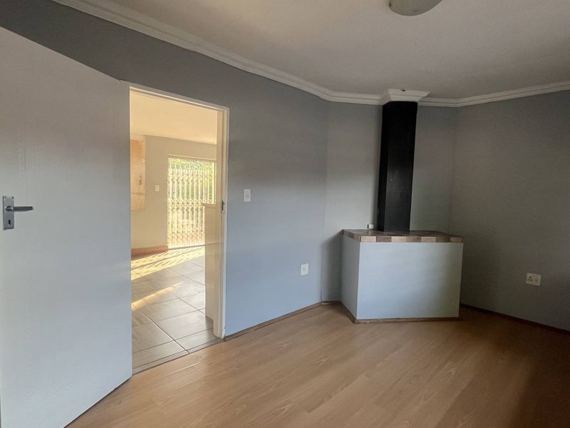 An empty living room featuring laminate flooring, a built-in fireplace, and neutral grey walls, with an open doorway leading to an adjacent tiled area.