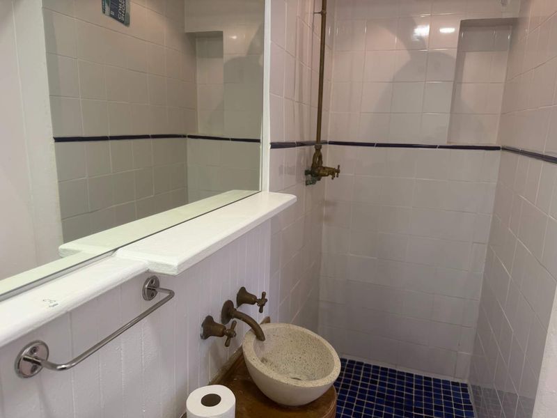A compact bathroom featuring a wall-mounted stone basin, brass fixtures, and a tiled shower enclosure with a built-in mirror.