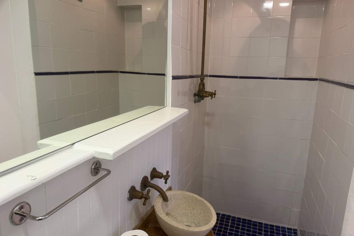 A compact bathroom featuring a wall-mounted stone basin, brass fixtures, and a tiled shower enclosure with a built-in mirror.