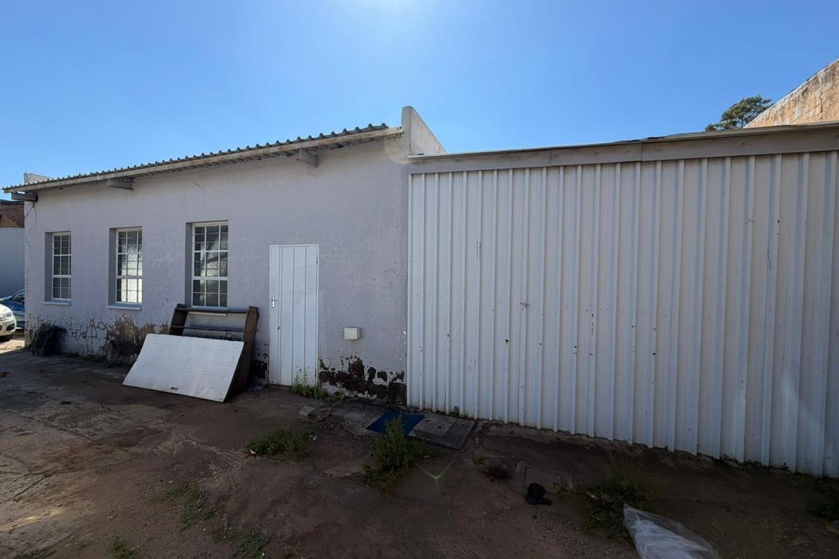 Rear exterior view of a commercial building featuring corrugated metal siding, weathered plaster walls, and multiple windows requiring maintenance and repair.