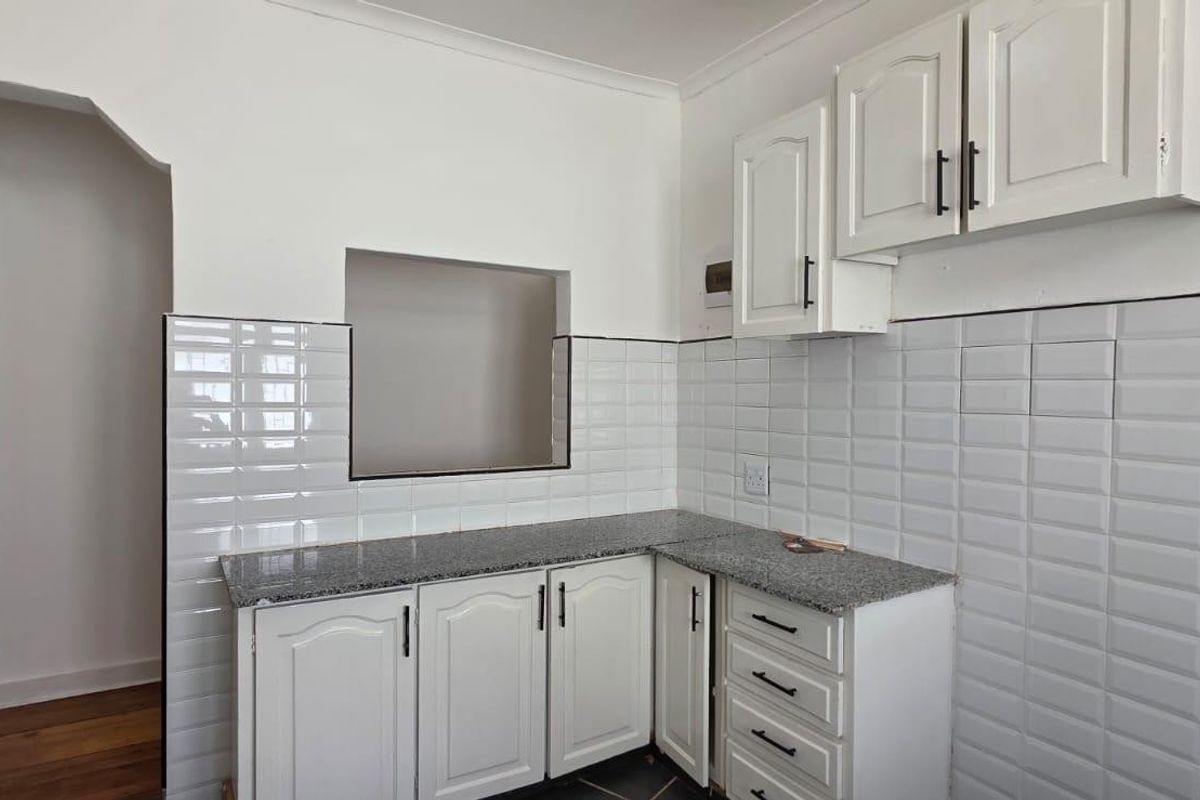 A clean, functional kitchen featuring white shaker-style cabinetry, granite countertops, and a classic white subway tile backsplash with a convenient pass-through window.