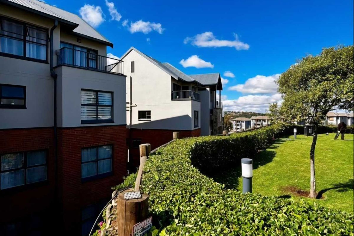 Exterior view of a multi-story townhouse complex featuring brick and rendered facades, balconies, and well-maintained communal garden areas.