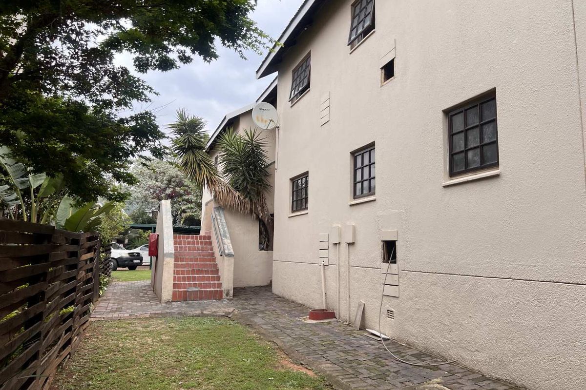 Rear exterior view of the apartment building featuring a paved walkway, external staircase, and satellite dish installation.