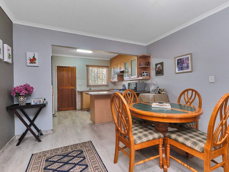 Open-plan dining area flowing into a functional kitchen with wooden cabinetry, laminate flooring, and a classic timber door.