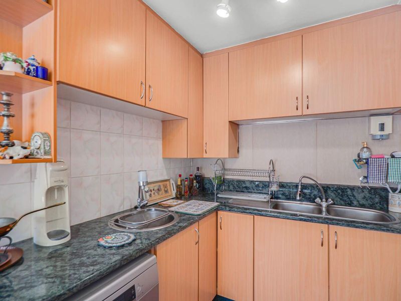 A functional kitchen featuring light wood-tone cabinetry, dark patterned laminate countertops, a double stainless steel sink, and tiled backsplash.