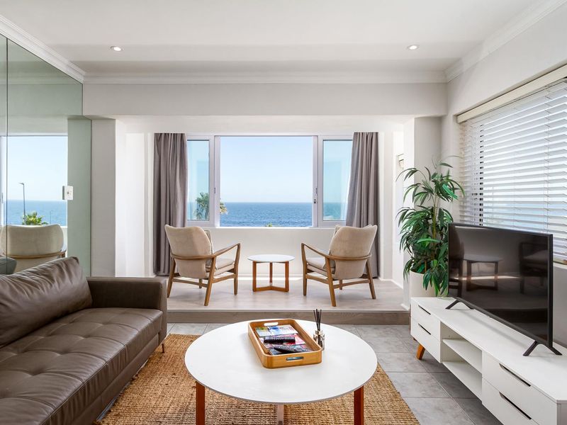 Bright living room featuring a raised platform area with expansive ocean views, tiled flooring, and modern recessed lighting.
