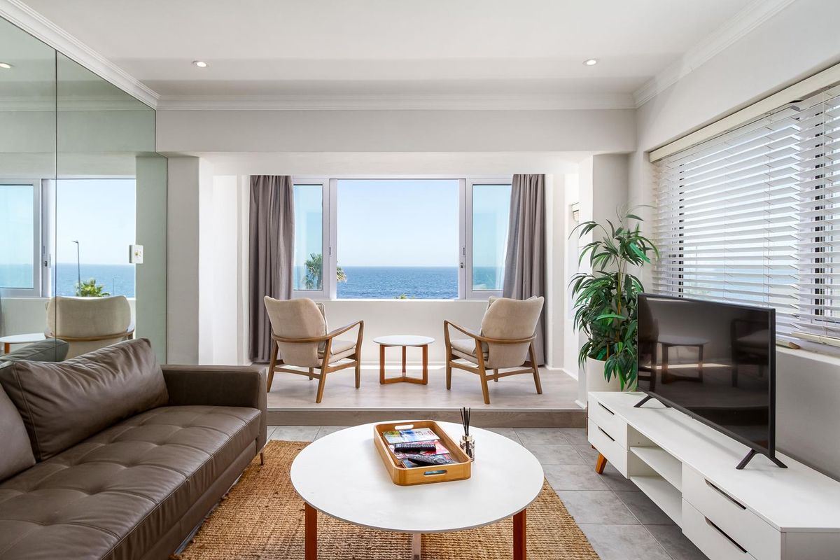 Bright living room featuring a raised platform area with expansive ocean views, tiled flooring, and modern recessed lighting.