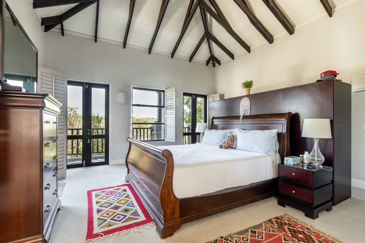 Spacious bedroom featuring high vaulted ceilings with exposed timber beams, neutral carpeting, and direct access to a private balcony through double doors.