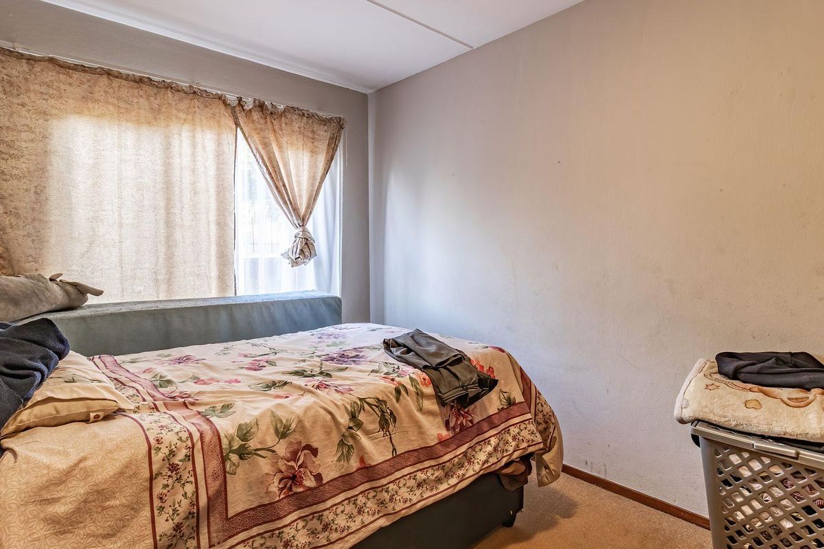 A bedroom featuring carpet flooring and a window, currently showing signs of wear on the wall surfaces.