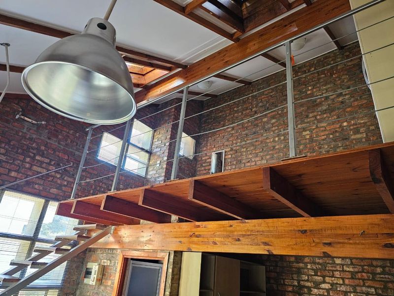 Spacious living area featuring industrial-style exposed brick walls, a timber mezzanine level with steel balustrades, and natural light from overhead skylights.