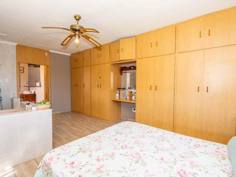 Spacious bedroom featuring extensive built-in wooden cabinetry, a ceiling fan, tiled flooring, and an integrated en-suite vanity area.