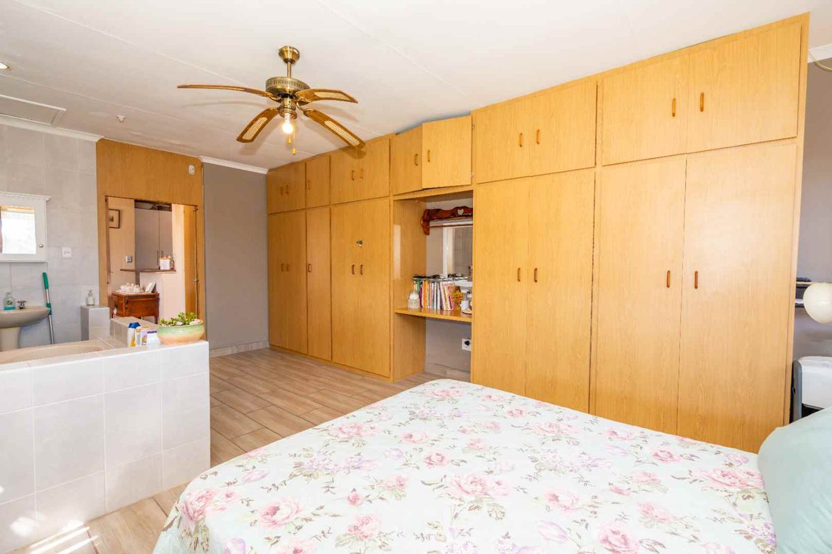 Spacious bedroom featuring extensive built-in wooden cabinetry, a ceiling fan, tiled flooring, and an integrated en-suite vanity area.