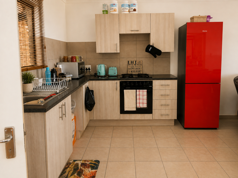 A functional kitchen featuring light wood-look cabinetry, dark countertops, a built-in oven with gas hob, and neutral tiled flooring.