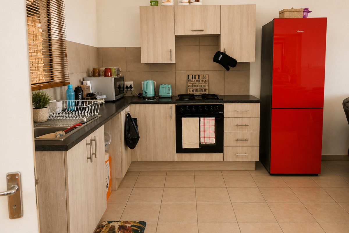 A functional kitchen featuring light wood-look cabinetry, dark countertops, a built-in oven with gas hob, and neutral tiled flooring.