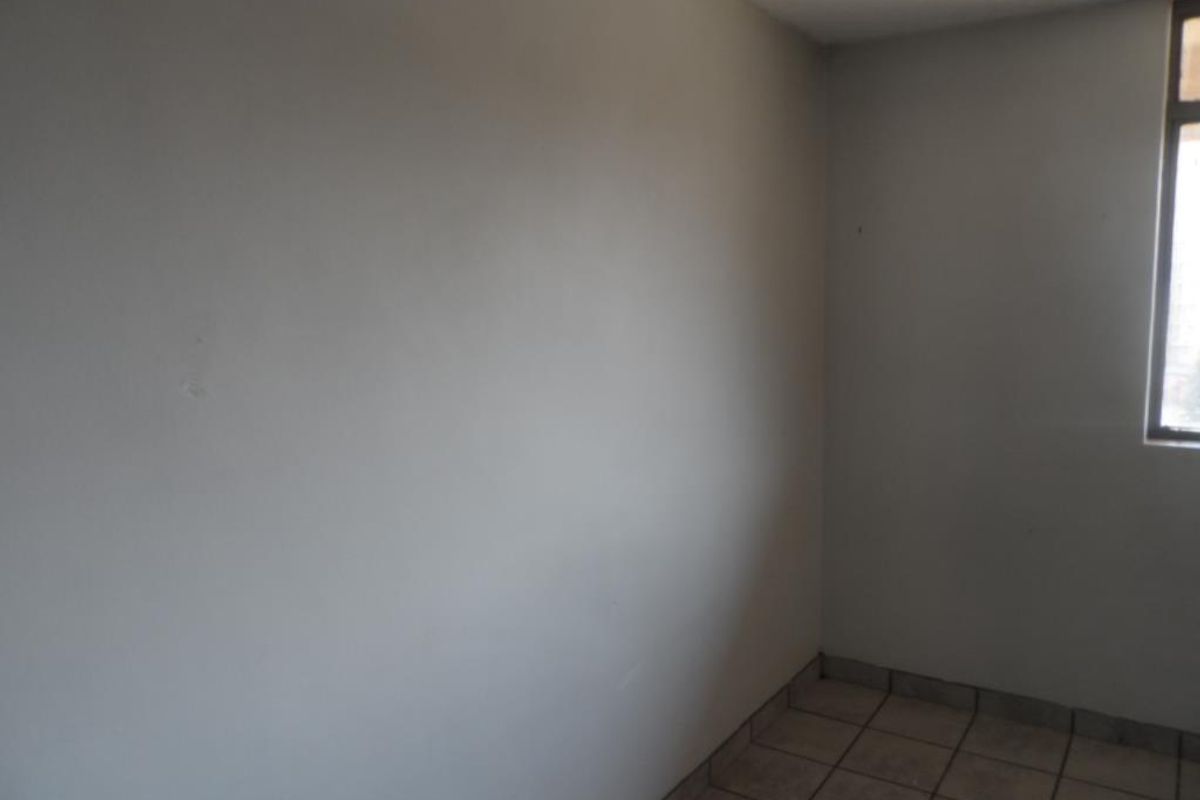 An empty bedroom featuring tiled flooring and a single window, requiring cosmetic updates to the wall finishes.