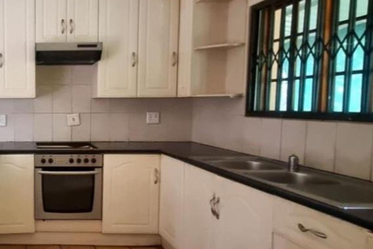 A functional kitchen featuring cream-colored cabinetry, a built-in oven with extractor fan, double sink, and tiled flooring.
