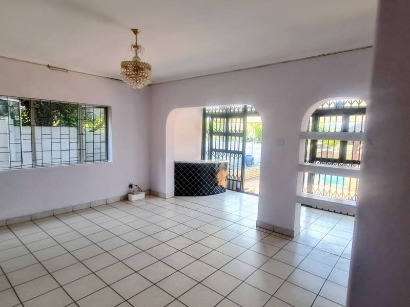 Spacious living area featuring tiled flooring, a built-in bar counter, and arched access to the outdoor area with security gates.
