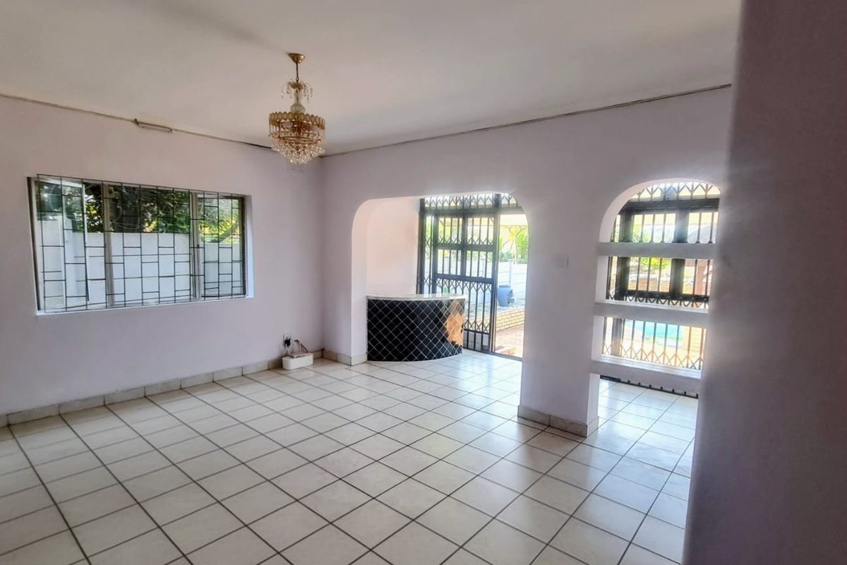 Spacious living area featuring tiled flooring, a built-in bar counter, and arched access to the outdoor area with security gates.
