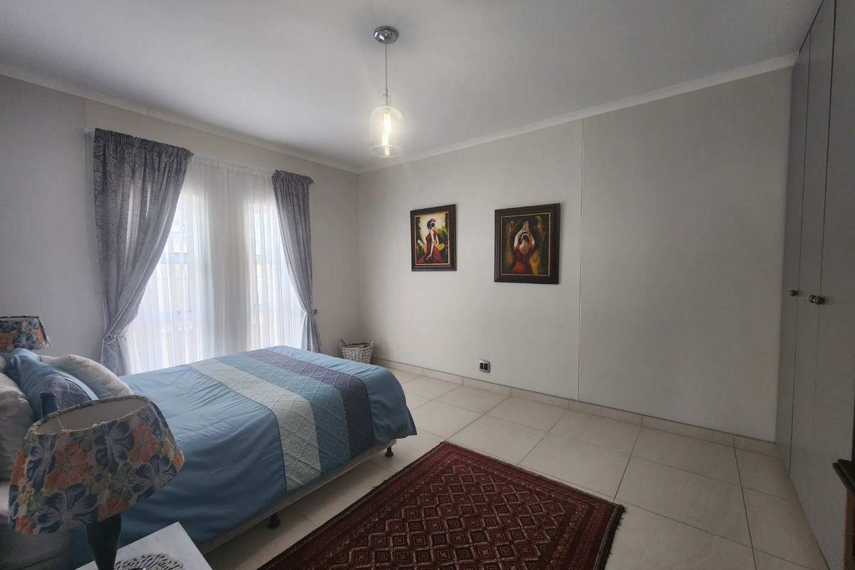 A well-lit bedroom featuring neutral tiled flooring, built-in cupboards, and large windows with curtains, providing a clean and functional living space.