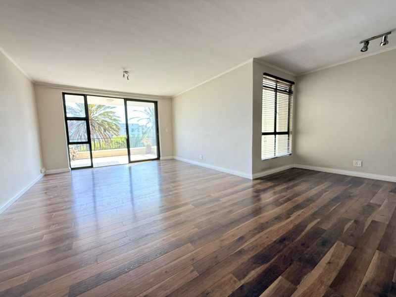 Spacious, light-filled living area featuring modern laminate flooring, large sliding doors leading to a balcony, and neutral wall finishes.