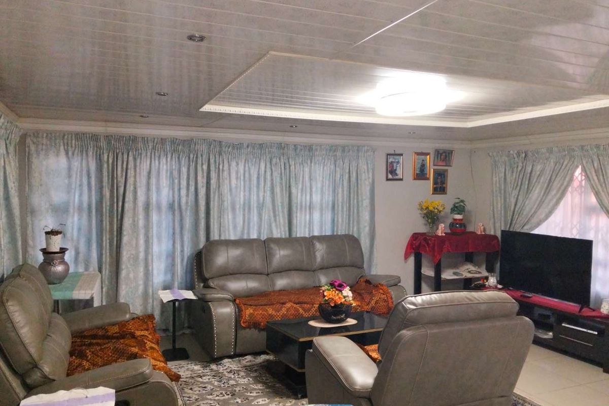 A comfortable living room featuring tiled flooring, a panelled ceiling with recessed lighting, and large windows dressed with curtains.