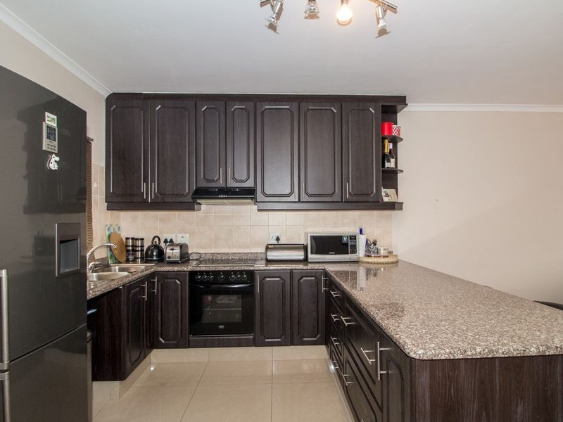 A functional kitchen featuring dark wood cabinetry, granite countertops, a breakfast bar, and built-in oven with extractor fan.