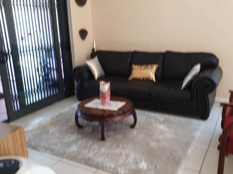 A living room featuring tiled flooring and a sliding glass door with an integrated security gate, providing access to the outdoor area.