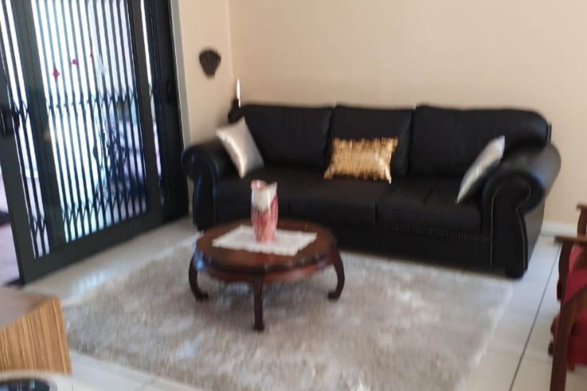 A living room featuring tiled flooring and a sliding glass door with an integrated security gate, providing access to the outdoor area.
