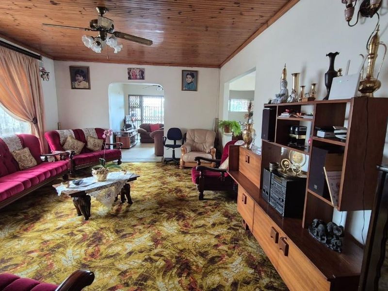 Spacious living room featuring a timber-paneled ceiling, ceiling fan, and patterned carpet flooring, with an open archway leading to an adjacent living area.