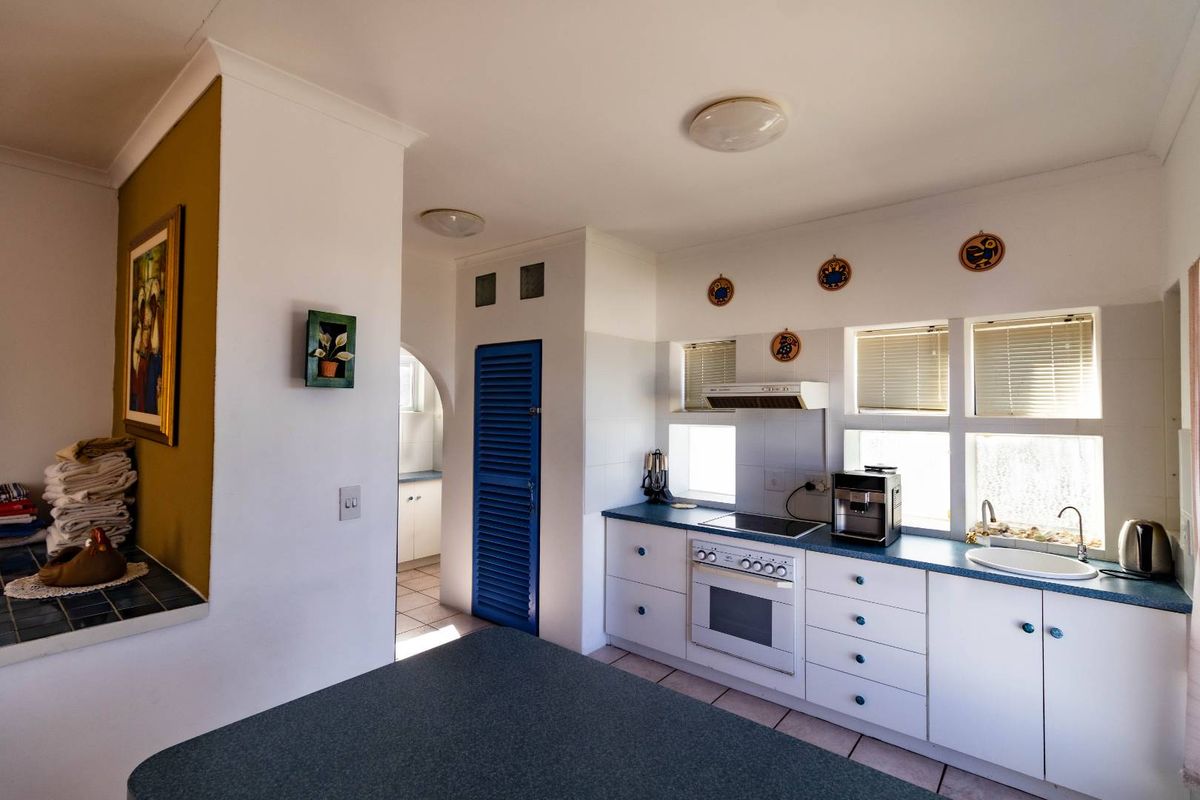 A functional kitchen featuring white cabinetry, blue laminate countertops, built-in oven, electric cooktop, and tiled flooring with an adjacent scullery area.
