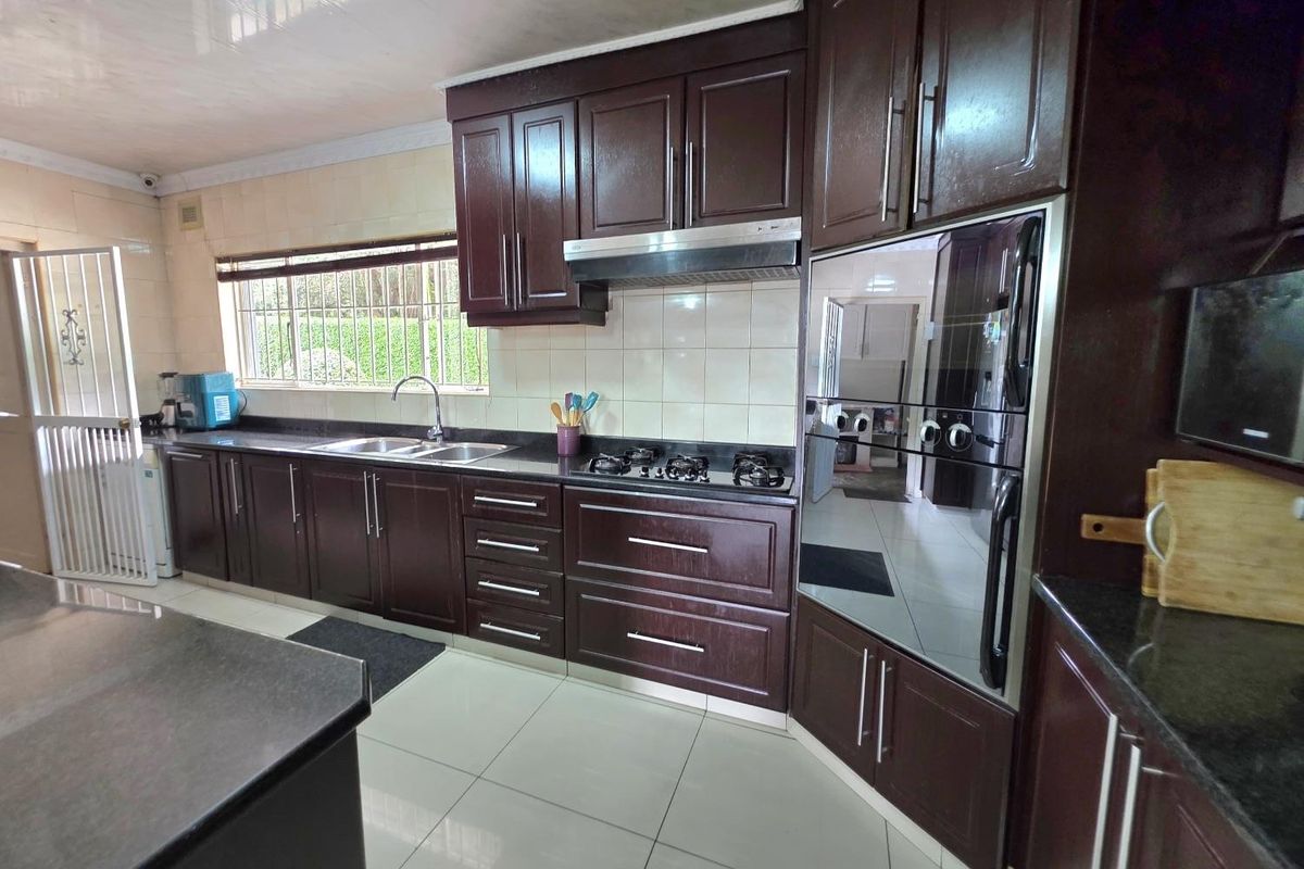 A functional kitchen featuring dark wood cabinetry, granite countertops, a built-in oven, gas hob, and tiled flooring with a double sink.