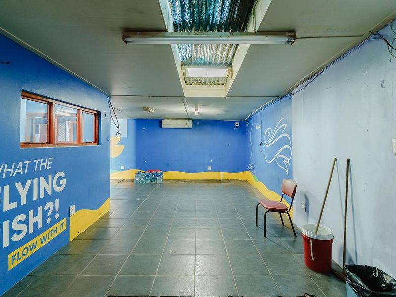 A spacious utility area featuring tiled flooring, a skylight, and a wall-mounted air conditioning unit, currently used as a multi-purpose storage or activity space.