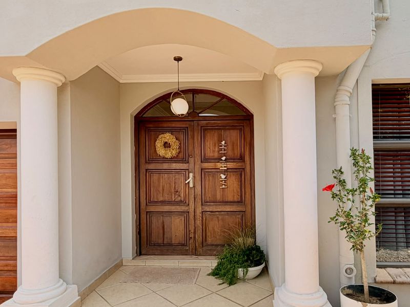 A welcoming front entrance featuring a covered portico with classical columns, a solid timber double door, and a decorative fanlight window.