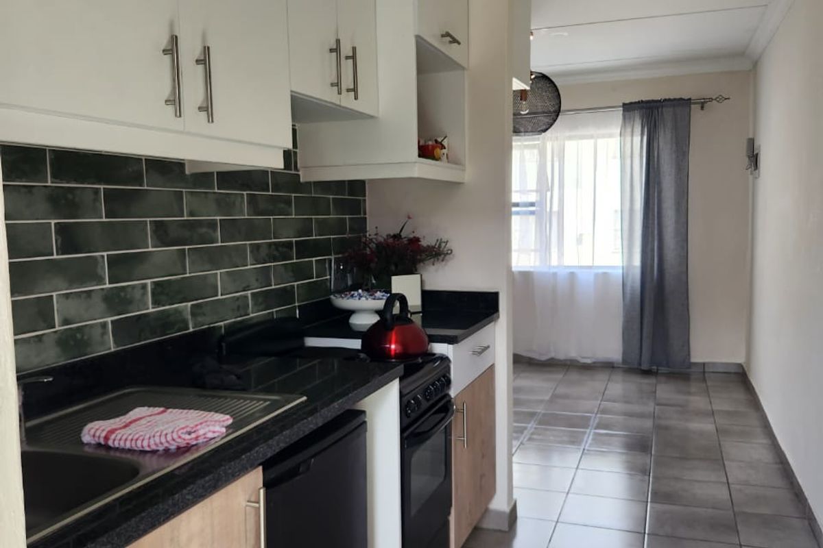 A functional kitchen featuring modern white and wood-tone cabinetry, black stone countertops, and a stylish dark green subway tile backsplash with tiled flooring.