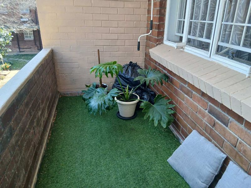 A compact balcony area featuring brick walls, security bars on the window, and artificial grass flooring.