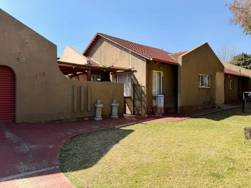 Front elevation of a single-story house featuring a tiled roof, paved driveway, and a covered patio area with a front garden.