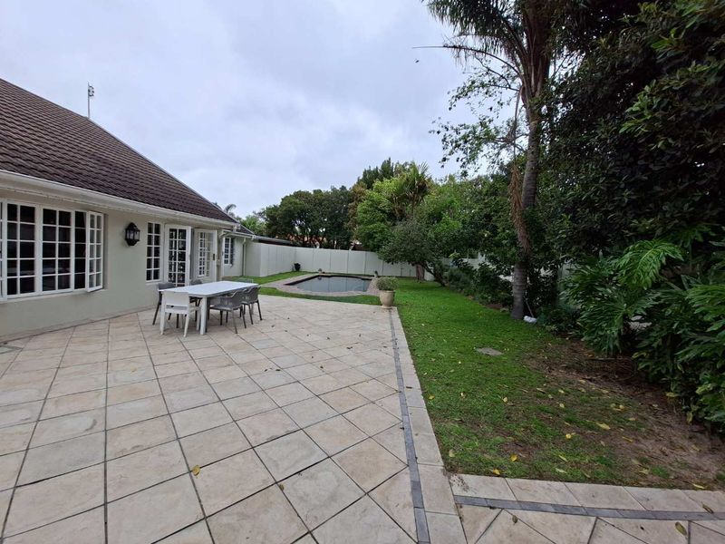 Spacious rear garden featuring a tiled patio area, a swimming pool, and established landscaping, providing a private outdoor entertainment space.