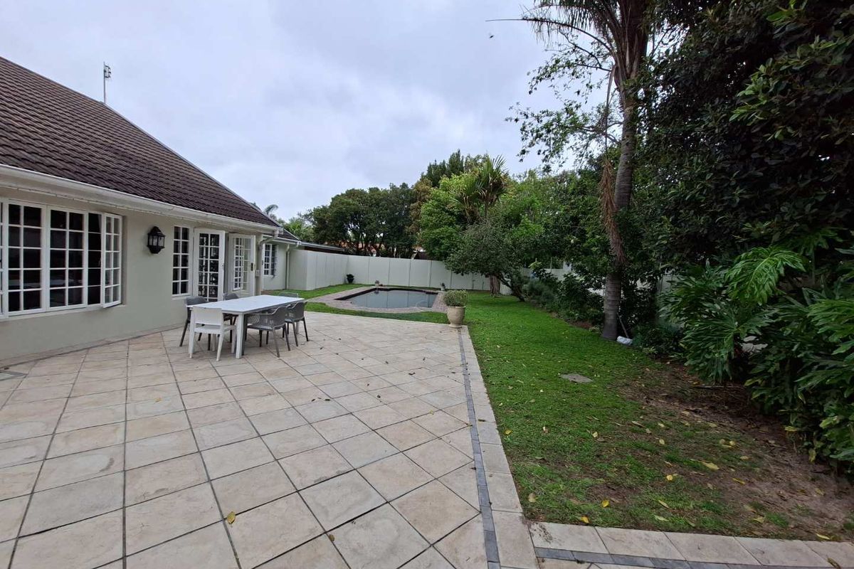 Spacious rear garden featuring a tiled patio area, a swimming pool, and established landscaping, providing a private outdoor entertainment space.