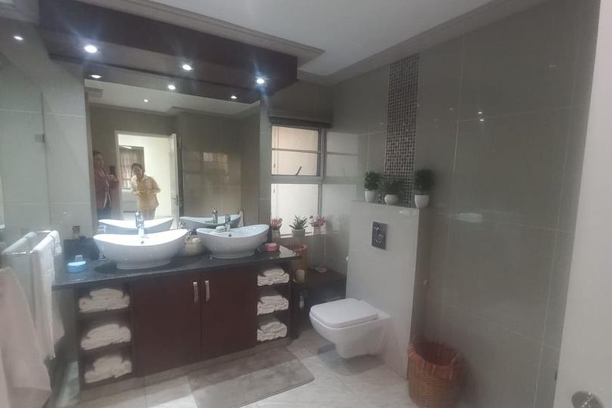 Modern bathroom featuring a double vanity with vessel sinks, wall-mounted toilet, bidet, and large mirror with integrated lighting.