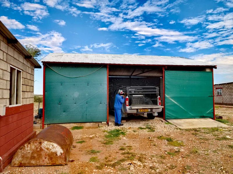 A functional farm garage structure featuring a corrugated metal roof, steel frame, and open-sided design with protective shade cloth screens.