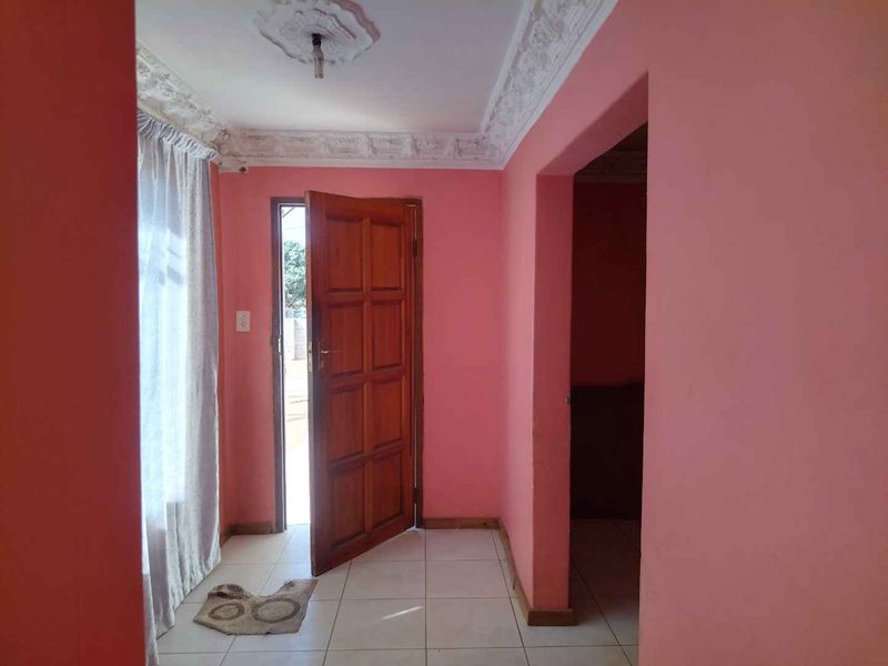 An entrance hall featuring tiled flooring, decorative ceiling cornicing, and a timber panelled door leading to the exterior.